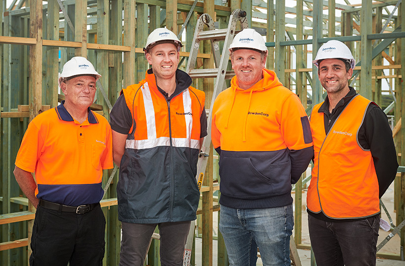 Photograph of 4 male Site Managers on a building site wearing PPE smiling at camera